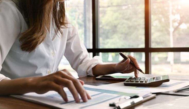 A woman sitting at a table, looking at paperwork and using a calculator.